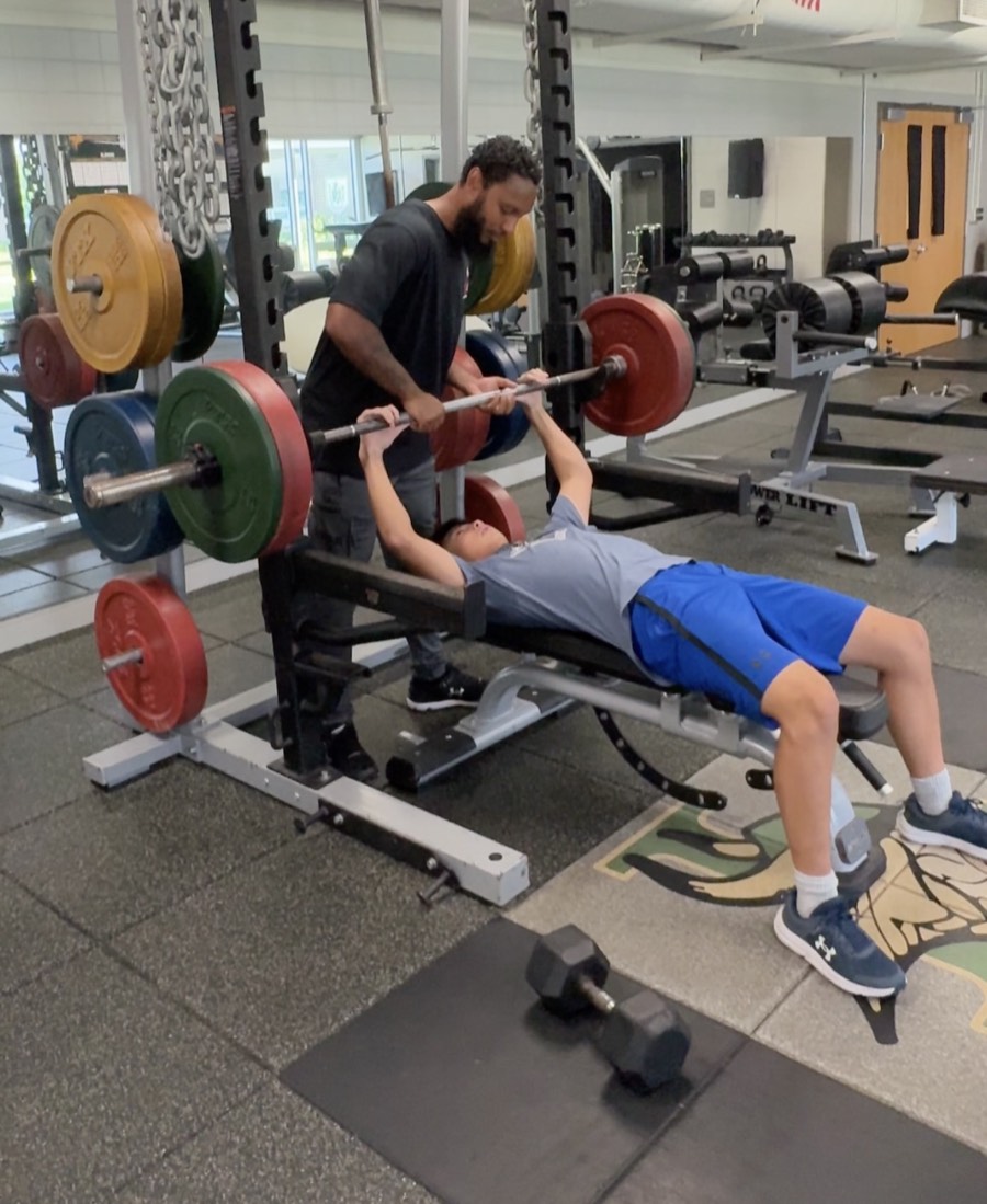Coach Hassan spotting an athlete through a barbell bench press in the weight room